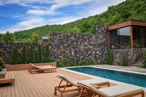 A wooden deck with lounge chairs and a swimming pool, surrounded by a stone wall and greenery. - Dilijani Tun (Dilijan)