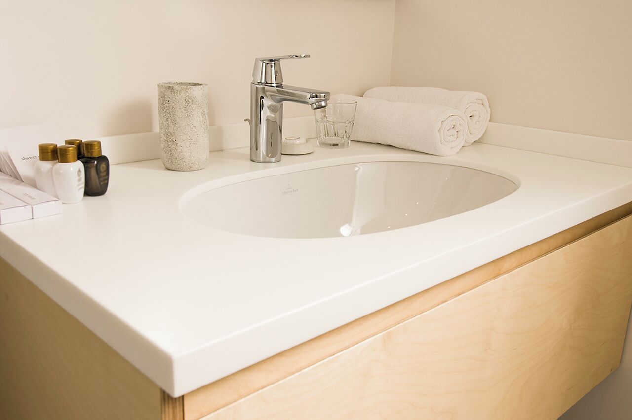 Un bagno con un lavandino bianco, un rubinetto moderno, un bicchiere e un asciugamano arrotolato.