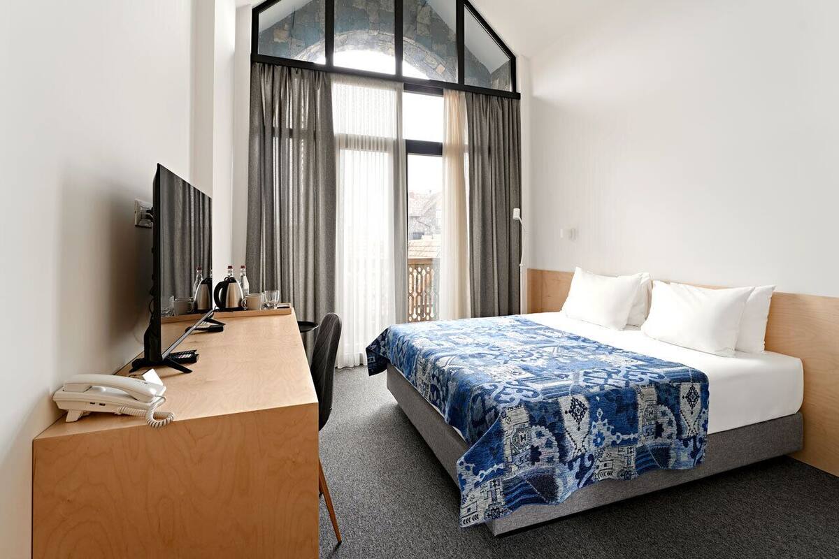 Ein Hotelzimmer mit einem Bett, einem Schreibtisch mit Telefon, einem Sessel und einem Fernseher.