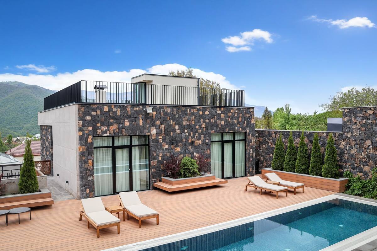 Ein modernes Gebäude mit Pool, Holzterrasse und Liegestühlen.
