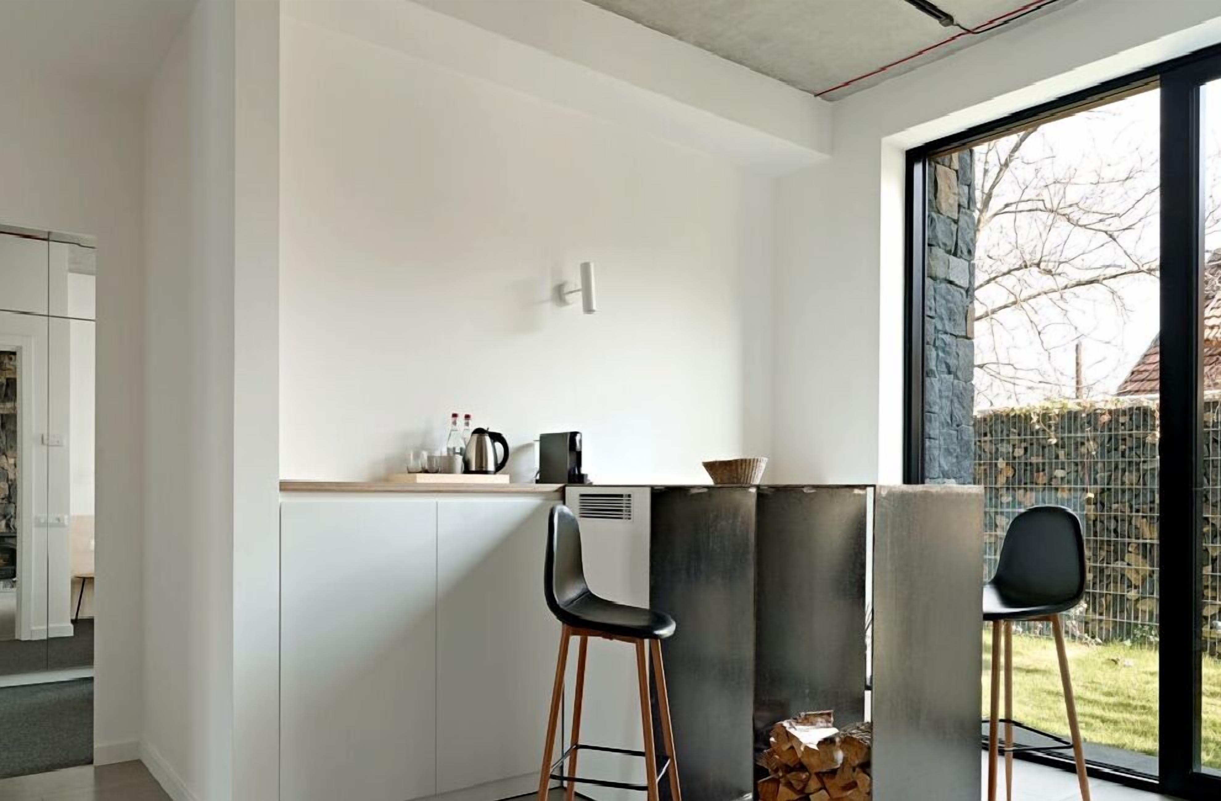 A modern kitchen with white cabinets, a bar stool, and a window with a view of a tree and a building.