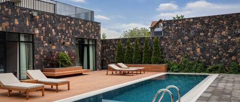 Una piscina moderna al aire libre con sillones de descanso y un muro de piedra.