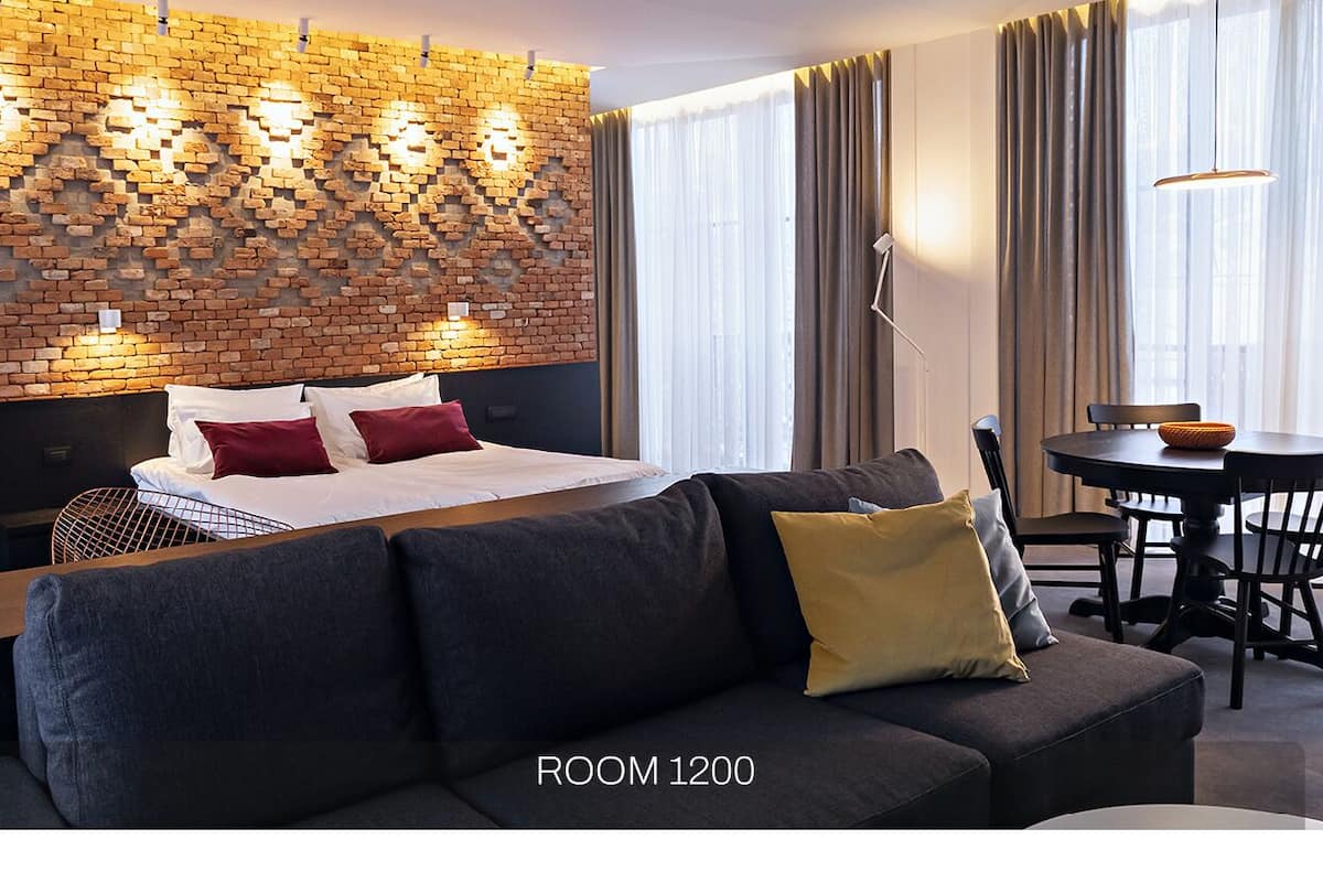 Ein modernes Hotelzimmer mit Ziegelwand, einem großen Bett, einer Couch, einem Esstisch und einer Kristallleuchtre.