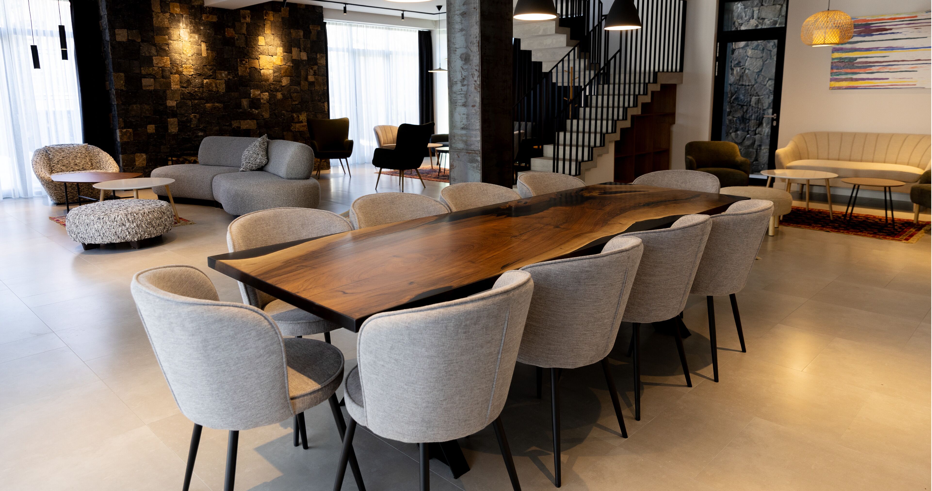A spacious room with a large wooden table surrounded by chairs, a staircase, and a stone wall.