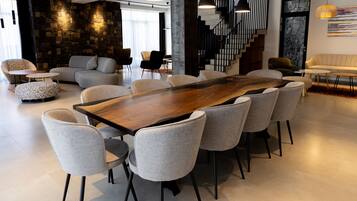 A spacious room with a large wooden table surrounded by chairs, a staircase, and a stone wall.