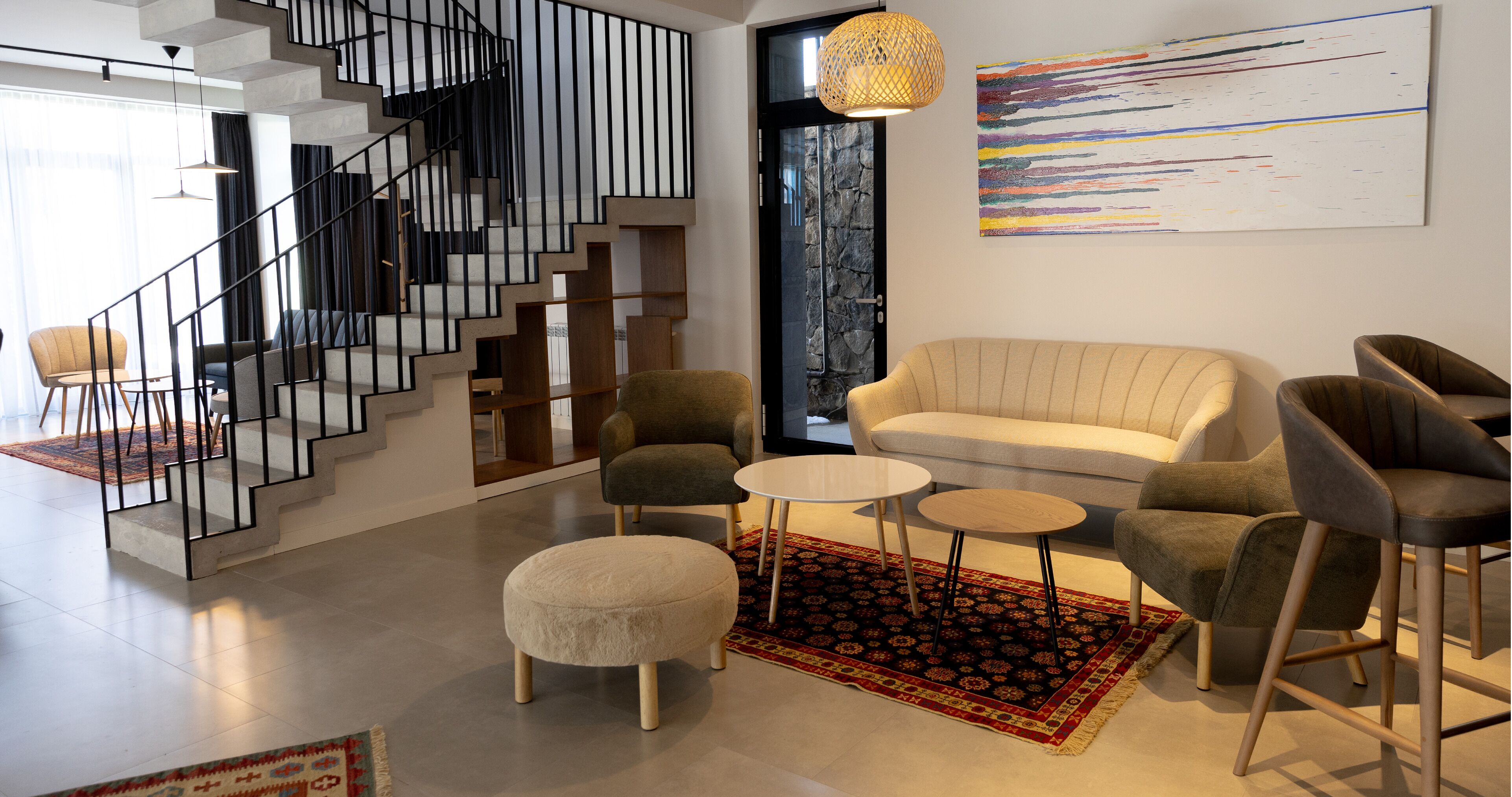 Een moderne woonkamer met een trap, een bank, een poef en fauteuils.