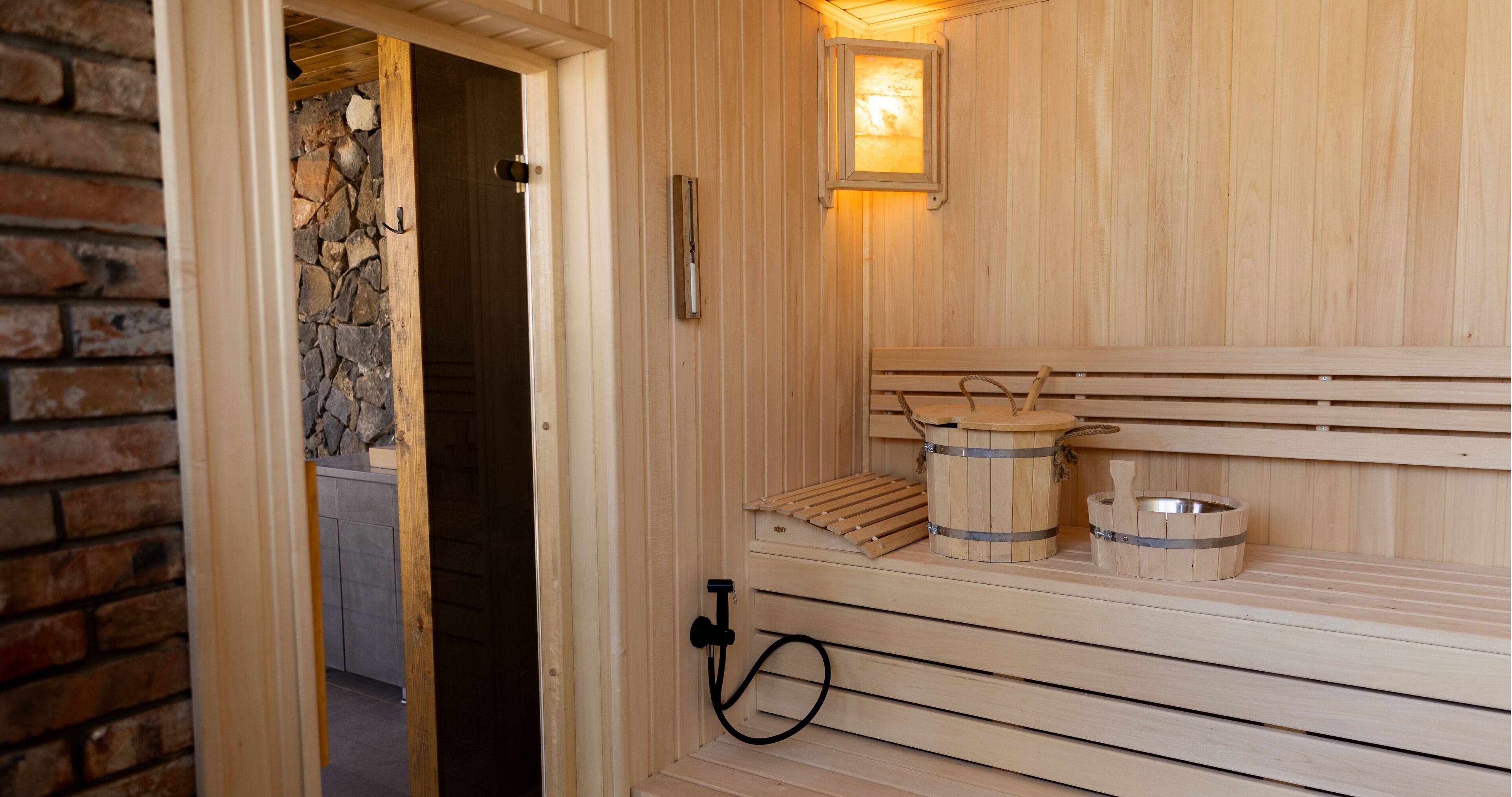 Una sauna de madera con bancos, un muro de piedra y un ventanal.