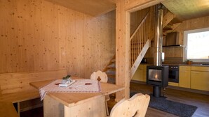 A wooden cabin interior with a dining table, chairs, a kitchen area with a stove, and a staircase. - Nice chalet with infrared sauna (Sankt Georgen am Kresichberg)