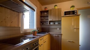 A compact kitchen with wooden cabinets, a built-in microwave, and a stove. - Nice chalet with infrared sauna (Sankt Georgen am Kresichberg)