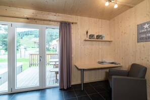 A wooden interior with a sliding glass door leading to an outdoor deck, a table with magazines, a chair, and a shelf with decorative items. - Appealing chalet with hot tub (Kreischberg Murau)