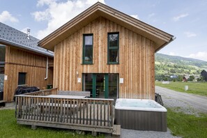 Een houten gebouw met een schuin dak, twee ramen, een deur en een hottub ervoor.
