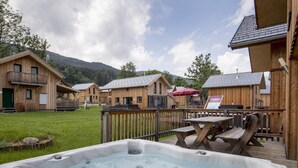 A wooden cabin with a hot tub, deck, and picnic table.