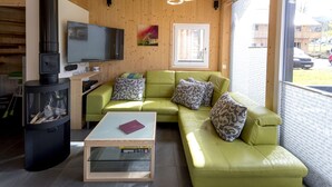 Una sala de estar acogedora con un sofá verde, un televisor, una chimenea y un ventanal grande.