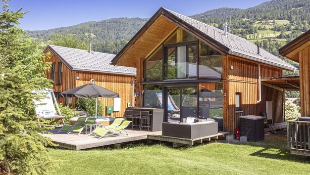 Una cabaña de madera con terraza, mobiliario exterior y un amplio ventanal.