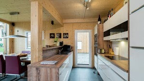 Una cocina moderna con detalles de madera, un comedor con sillas rojas y vistas a través de un ventanal.