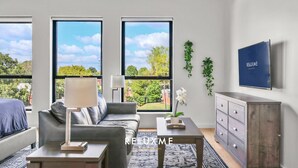 A modern living room with a grey sofa, a coffee table, and a TV on the wall. - Reluxme|European Flat Near Uptown King Bed + Views (Charlotte)