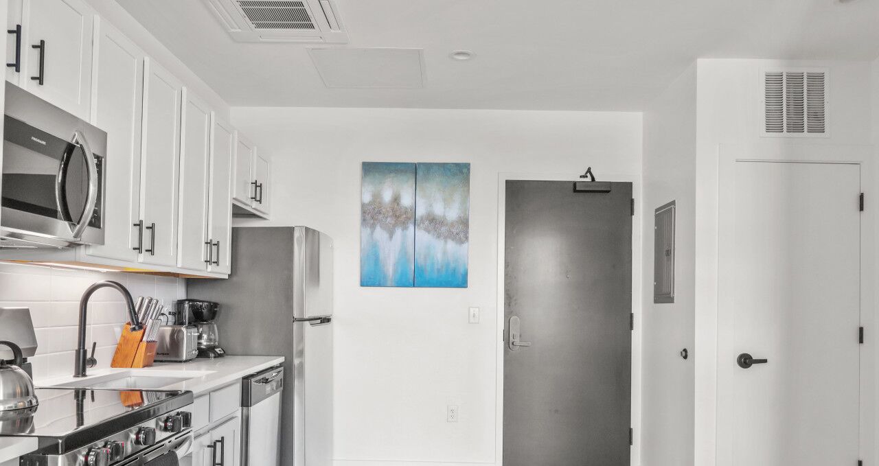 A modern kitchen with white cabinets, stainless steel appliances, and a painting on the wall.