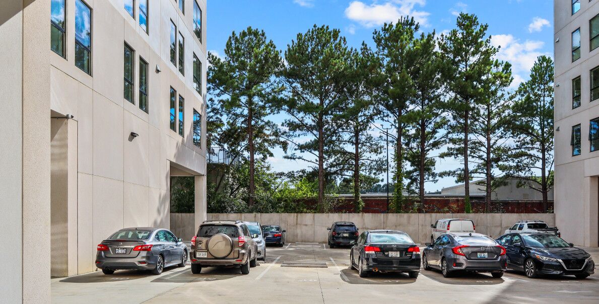 Un parking avec plusieurs voitures et un bâtiment doté de nombreuses fenêtres et d’un mur en béton.