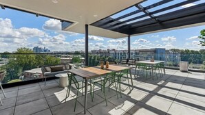 A rooftop terrace with a table and chairs, a grill, and a view of the city skyline. - Reluxme|European Flat Near Uptown King Bed + Views (Charlotte)