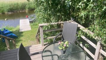 Una terraza de madera con una mesa y sillas de vidrio, con vista a una masa de agua rodeada de vegetación.