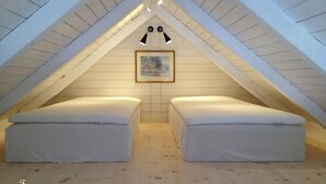 Ett litet sovrum på vinden med två vita sängar, träribbor i taket och en inramad tavla på väggen.