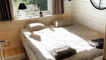 A single bed with a headboard, a window with curtains, a wall-mounted lamp, and a wooden floor.