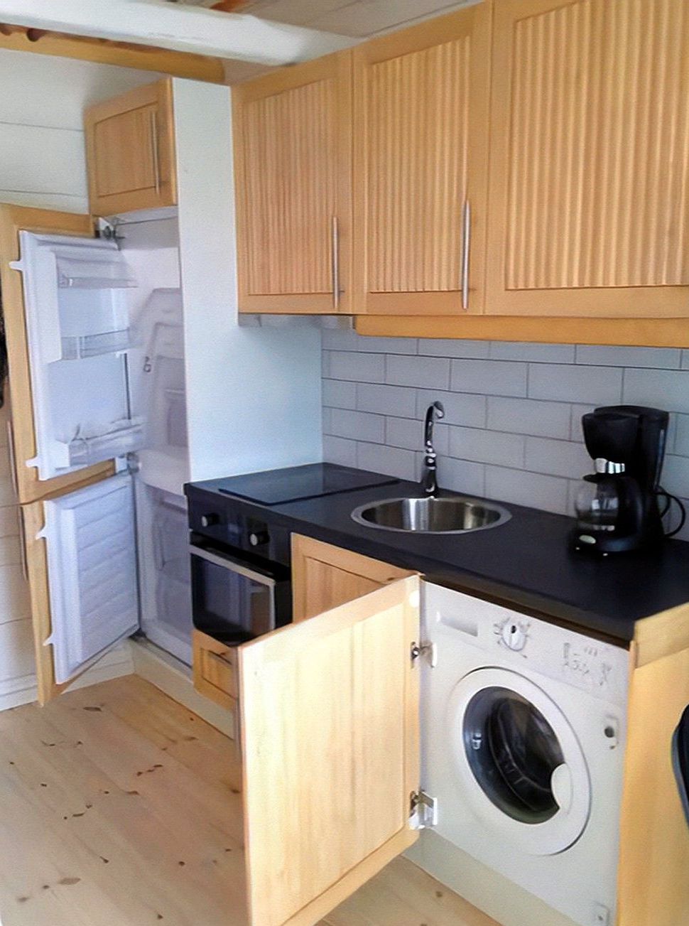 Een kleine keuken met houten kastjes, een inbouw wasmachine, een koffiezetapparaat en een koelkast.