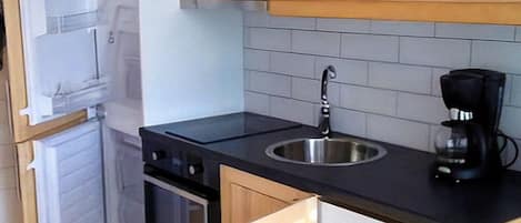 Une cuisine compacte avec des meubles en bois, un lave-linge encastré, une machine à café et un réfrigérateur.