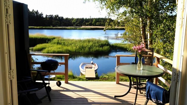 En terrass med utsikt över en sjö, en båt och utemöbler.