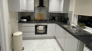 A modern kitchen with white cabinets, a stove, oven, sink, and a trash bin.