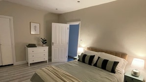 A bedroom with a bed, a nightstand, a dresser, a door, and a wall-mounted picture.