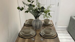 A dining table with a black and white striped vase, surrounded by beige plates and glasses, set on a wooden table with black metal legs.