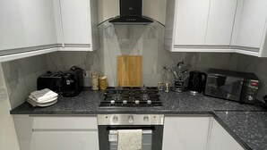 A modern kitchen with white cabinets, a black range hood, a gas stove, a microwave, and a coffee maker.