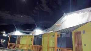A row of yellow buildings with metal roofs and wooden railings, under a night sky with a visible moon.