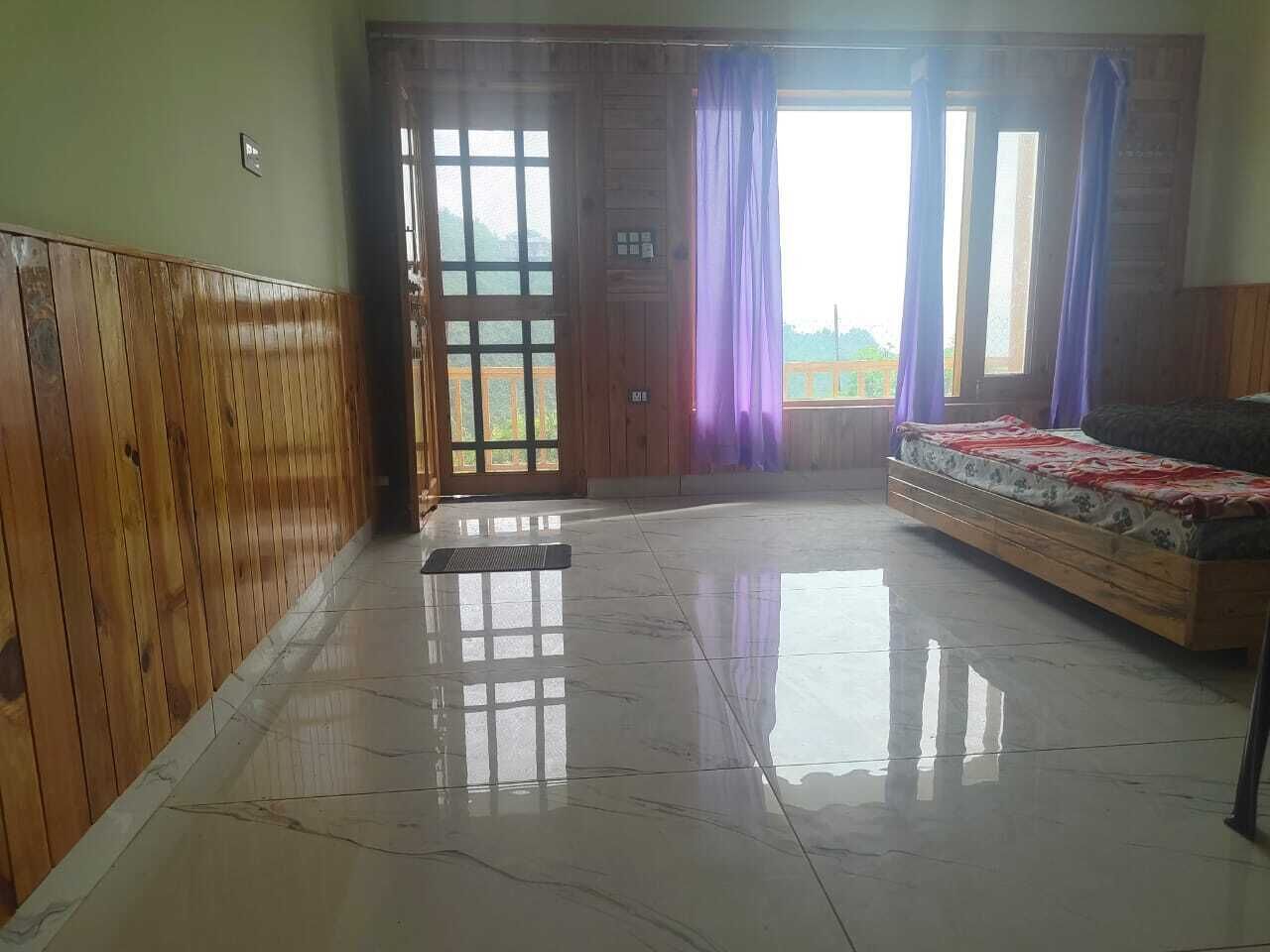 A spacious room with a wooden panel wall, a large window with purple curtains, a bed with a floral bedspread, and a tiled floor.
