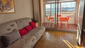 Ein Wohnzimmer mit einer Couch, roten Kissen, einem Gemälde und Blick auf eine Marina durch eine Schiebetür.