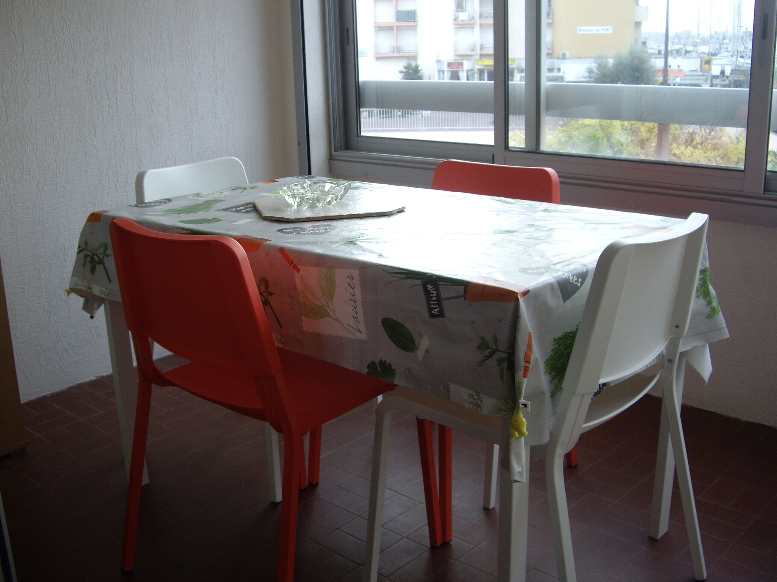 Una mesa de comedor con mantel floral, rodeada por cuatro sillas, una de ellas naranja.