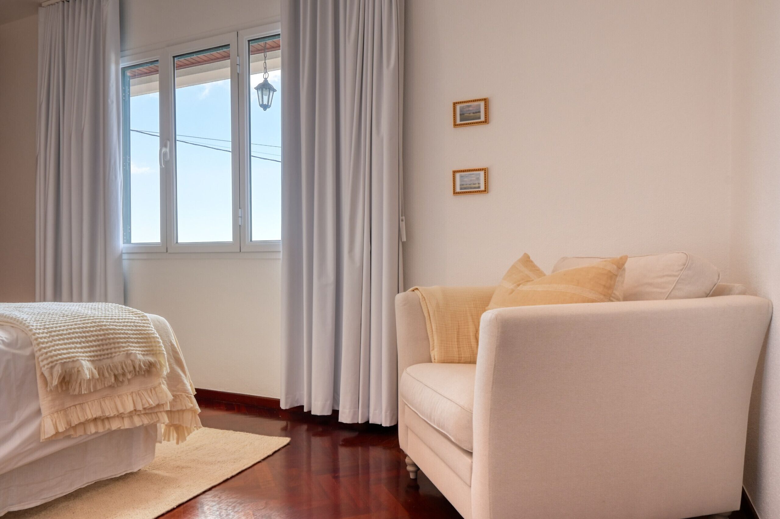 Ein Zimmer mit einem Bett, einem Schlafsofa, einem Fenster mit Vorhängen und zwei gerahmten Bildern an der Wand.