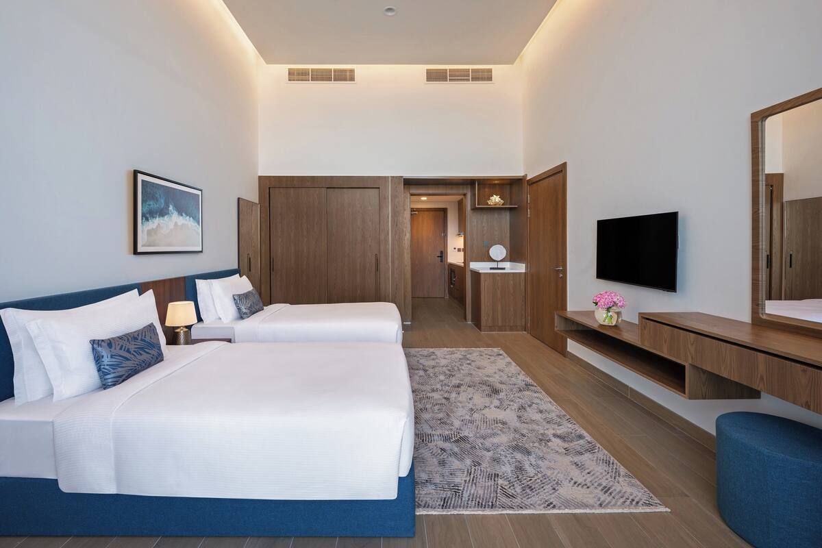 A hotel room with two beds, a TV, a mirror, and a desk with a vase of flowers.