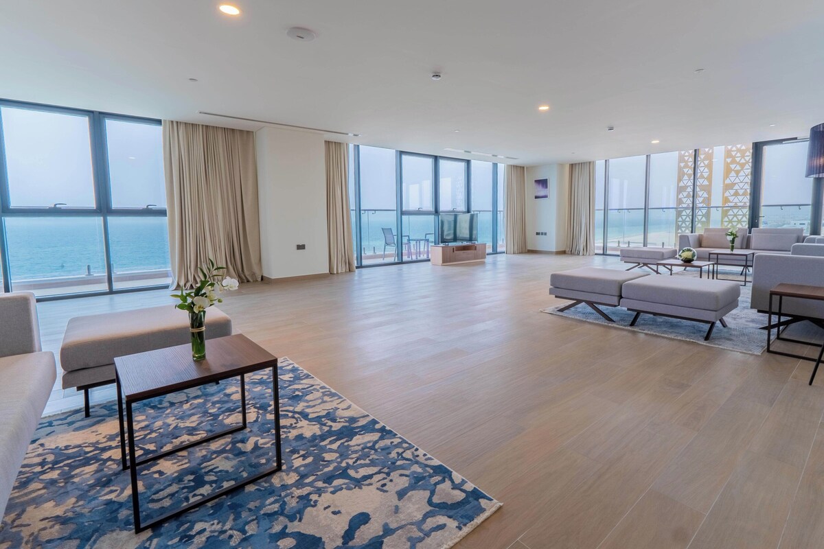 Un salón amplio con un gran ventanal con vistas al mar, un área de descanso confortable y un televisor de pantalla plana.