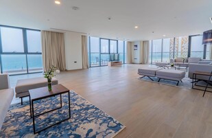 Uma sala de estar ampla com uma grande janela com vista para o mar, um espaço de estar confortável e uma televisão de tela plana.