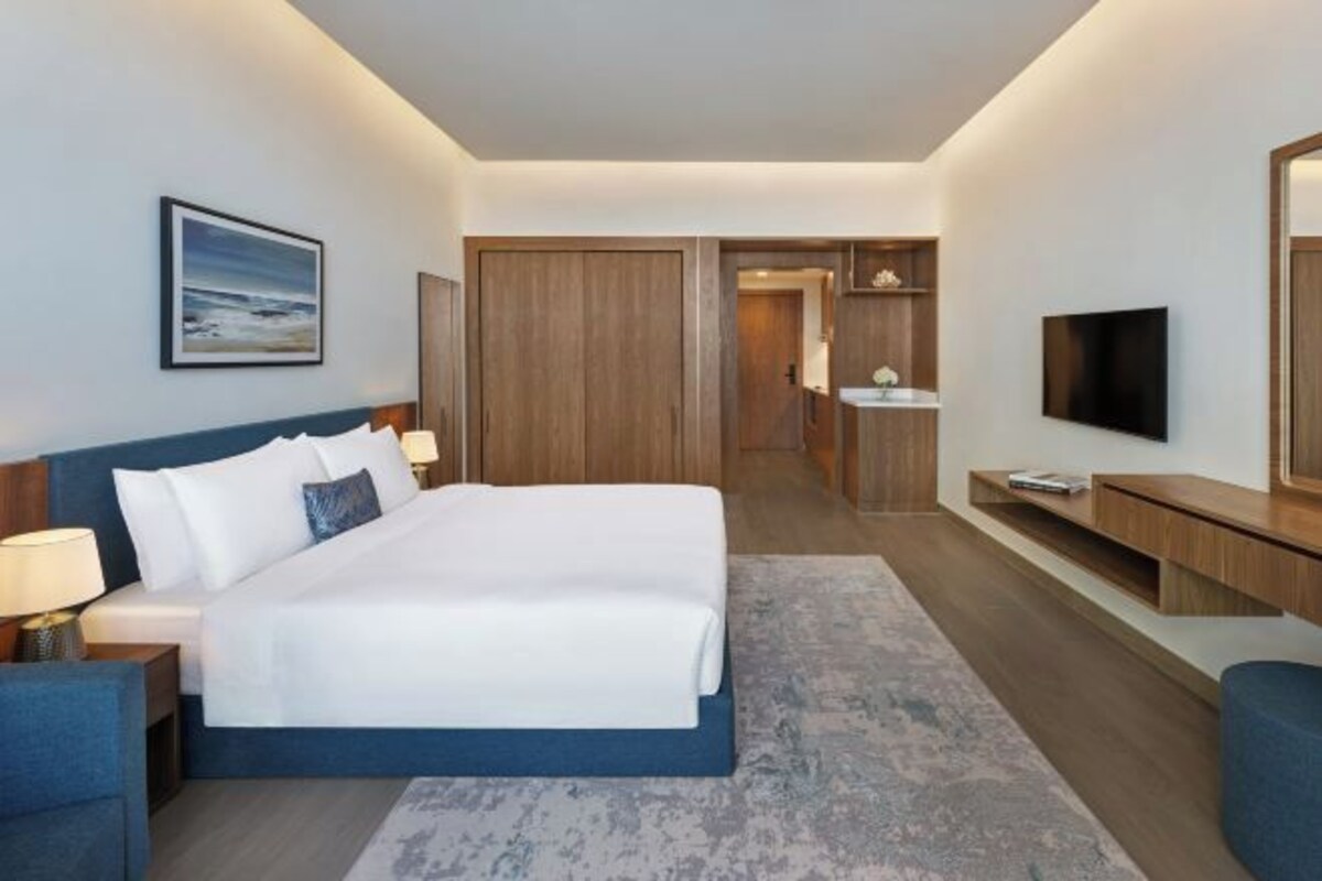 A hotel room with a large bed, bedside tables, a flat-screen TV, a mirror, and a bathroom with a sink and toilet.