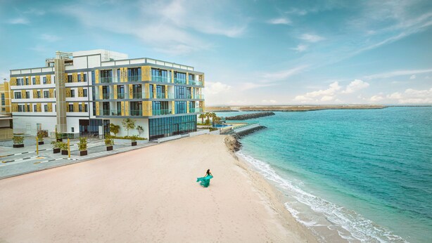 Un hotel frente a la playa con diseño moderno, con varios pisos, piscina y una playa de arena.