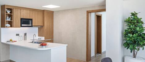 A modern kitchen with wooden cabinets, a white countertop, and a built-in microwave. There is a dining area with a table and chairs, and a potted plant on the right.