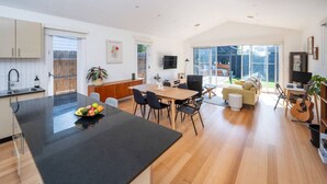 Une cuisine moderne avec un îlot central, un coin repas avec des chaises, un canapé et une guitare.