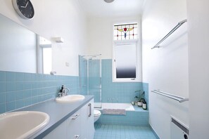 Et badeværelse med to vaske, en bruser, toilet og et vindue med farvet glas.
