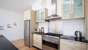 Une cuisine moderne dotée d’appareils électroménagers en acier inoxydable, de meubles de rangement en bois clair et d’un plan de travail noir.