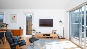 Un salon moderne avec une table basse en verre, un fauteuil en cuir noir, un meuble de rangement en bois et un téléviseur à écran plat fixé au mur.