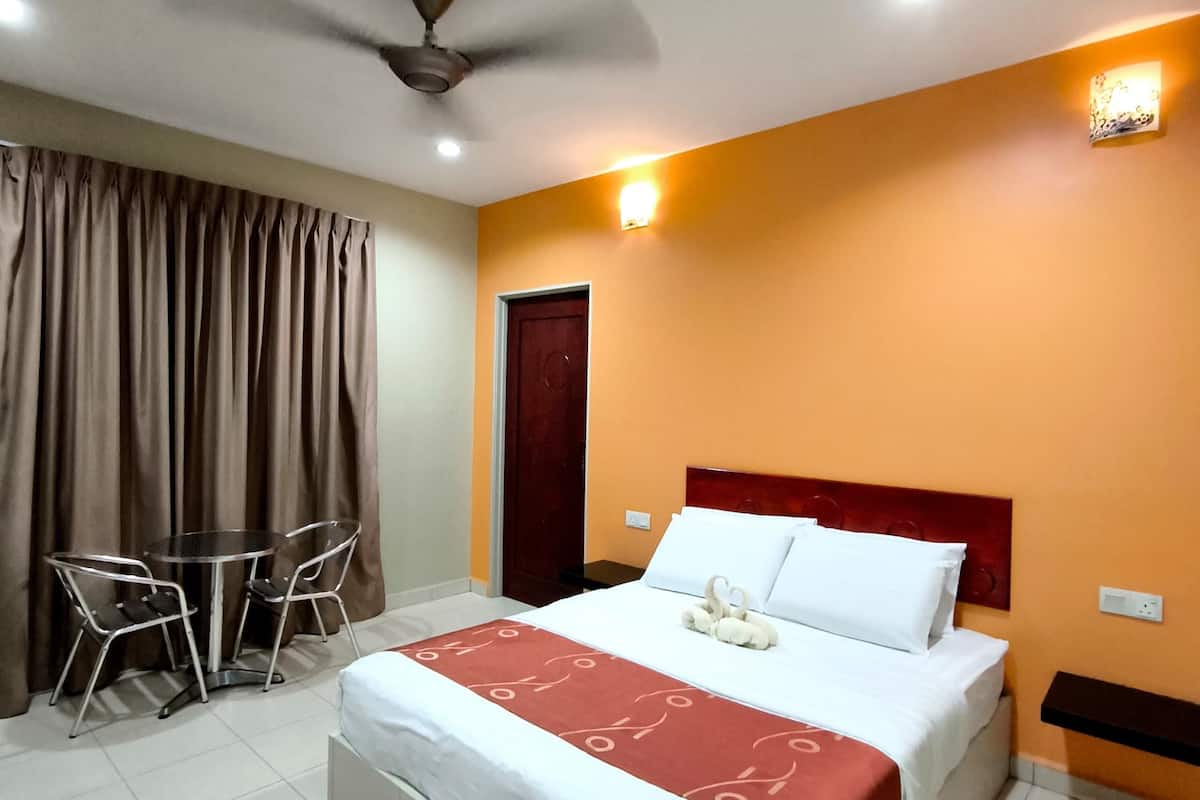 A hotel room with a bed, a desk, two chairs, a ceiling fan, and a door.
