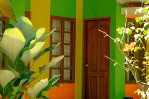 A building with a green and yellow facade, a wooden door, and a window with a curtain. - Casa Felicisima Inn (Puerto Princesa)